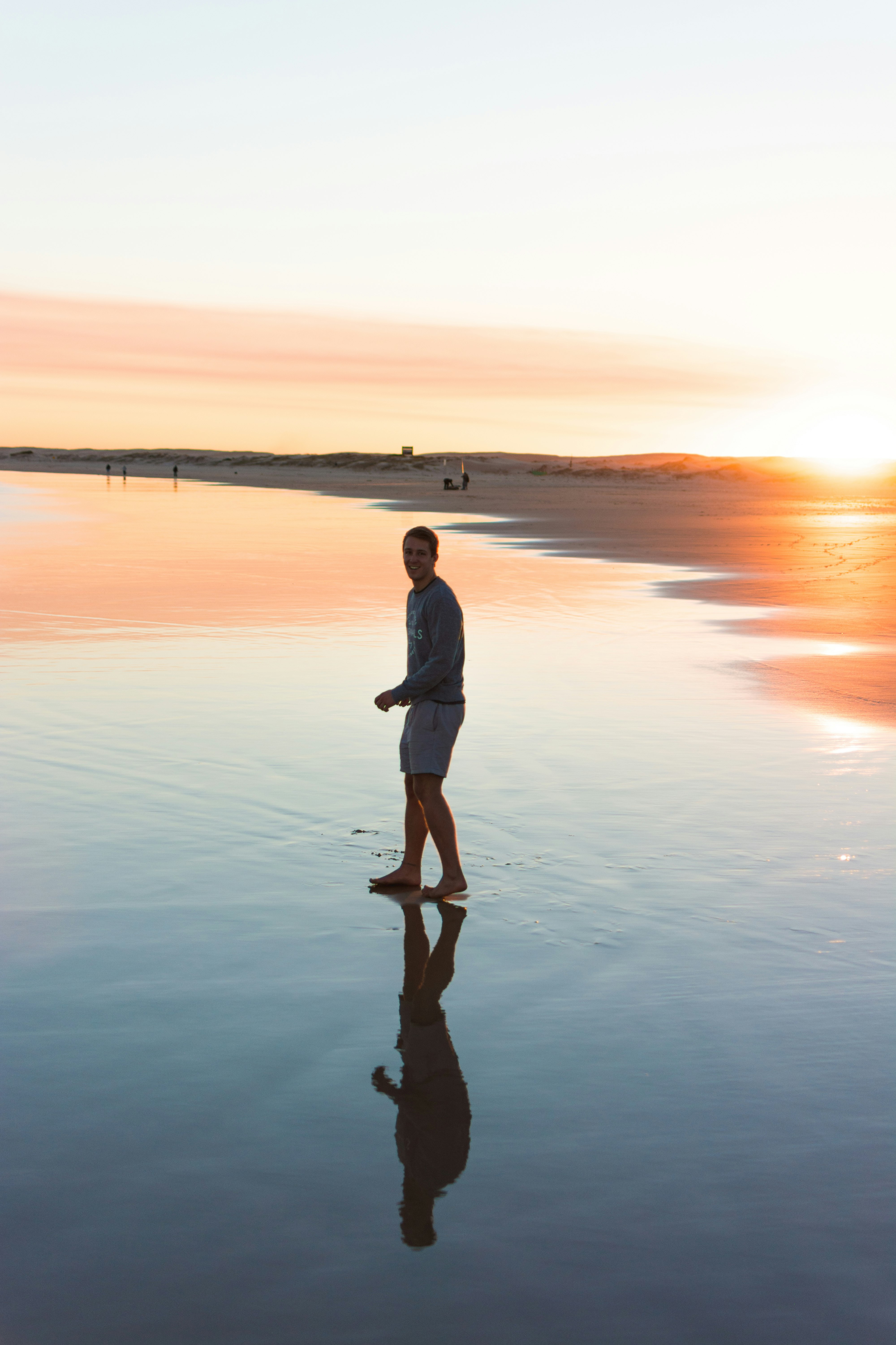 man in white long sleeve shirt and black pants standing on seashore during sunset